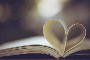 Close up heart shape from paper book on wooden table with vintage blur background photo