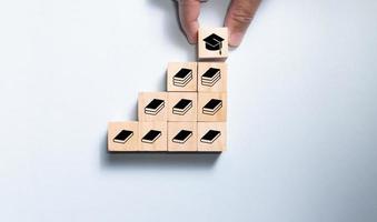 Top view wooden blocks set to step with book icon to graduate icon. Concept for learning and education.