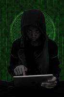 Hacker boy are hacking through the tablet on green symbols background. photo