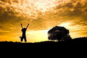 The silhouette of the woman jumping before sunrise with tree in the background photo