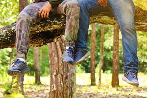 The leg part of  two men sit on the big branch of the tree in the forest photo