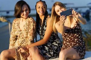 Cheerful diverse girlfriends taking selfie on smartphone in sunny day photo