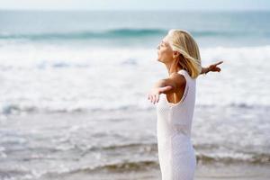 Mature woman opening her arms on the beach, spending her leisure time, enjoying her free time photo