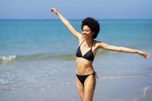 Happy black woman opening her arms on the beach to enjoy her holiday in the sun. photo