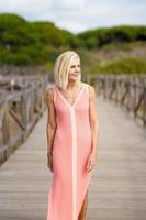 Beautiful mature woman walking along a wooden path near the beach., wearing a nice orange dress. photo