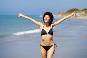 Cute black woman opening her arms on the beach to enjoy her holiday in the sun. photo