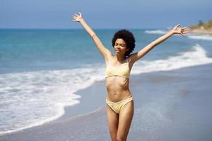 Positive black woman opening her arms on the beach to enjoy her holiday in the sun. photo