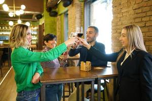 Diverse friends clinking glasses over table in beautiful pub photo