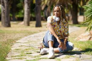 African woman with skateboard relaxing after riding skateboard outdoors. photo