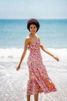 Happy black woman in summer dress, walking on the sand of a tropical beach. photo