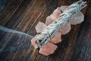 burning a smudge sage stick on a base of pink salt crystals with smoke trail photo