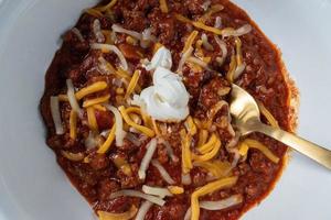 homemade chili with cheese and sour cream in bowl flat lay photo