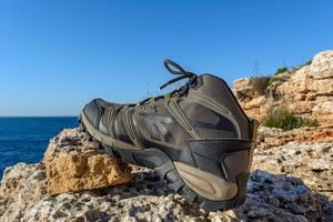 Olive green hiking boots on a natural background of sea and rocks photo