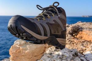 Olive green hiking boots on a natural background of sea and rocks photo