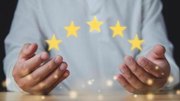 concepto de revisión del cliente. encima de las manos, hay cinco estrellas por un trabajo excelente. primer plano con el hombre de camisa blanca y bokeh dorado. foto