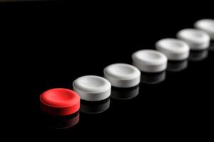 Behind the red pill are lined up white pills. One red and many white pills on a black background. With blur in perspective. Concept on leadership and features. photo