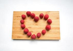 Tasty juicy ripe fresh red raspberry berries in the heart shaped form on a wooden cutting board photo