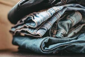 Stack of jeans various shades, empty space, horizontal photo on blurred background. Folded cloth, denim texture, fashionable, pile of different blue jeans