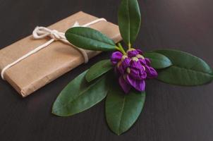 Purple azalea flower next to a gift in craft packaging photo