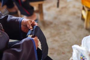 Close-up of hands old woman sew a button with a needle. photo