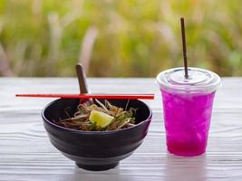 Close-up of noodle Soup in black cup with red chopsticks and herb water on white wooden table photo