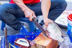 el trabajador está cortando pescado de tilapia en el mercado local. foto