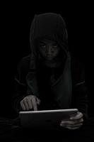 el chico hacker está pirateando la tableta en un fondo negro. foto