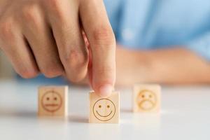 concepto de encuesta de satisfacción del cliente, la mano del cliente selecciona un cubo de madera con un icono de cara sonriente, la mejor calificación de excelencia de servicio para la satisfacción. foto