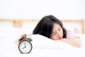 Beautiful asian young woman turn off alarm clock in morning, wake up for sleep with alarm clock, relax and lifestyle concept. photo