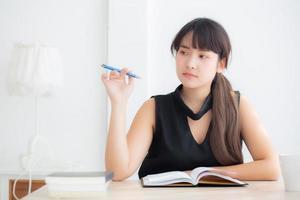 Young asian woman writer smiling thinking idea and writing on notebook or diary with happy on desk office, lifestyle of asia girl is success, female planning working, education and business concept. photo
