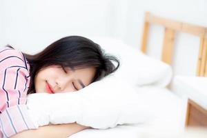 retrato de una hermosa joven asiática durmiendo en la cama con la cabeza en la almohada cómoda y feliz con el ocio, chica con relajación para el concepto de salud y estilo de vida. foto