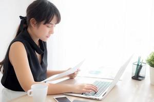 Young asian woman working and typing with laptop computer at office, businesswoman looking graph diagram analysis statistic data of finance, girl using notebook, profit growth, business concept. photo