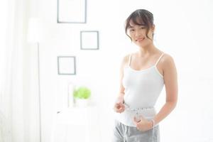 Beautiful young asian woman body diet and slim with measuring waist for weight in the bedroom, girl have cellulite and calories loss with tape measure, health and wellness concept. photo