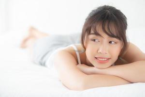 hermoso retrato joven mujer asiática acostada y sonriendo mientras se despierta con el amanecer en la mañana, belleza linda chica feliz y alegre descansando en la cama en el dormitorio, estilo de vida y concepto de relajación. foto