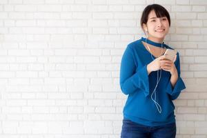 hermoso retrato mujer joven asiática de pie feliz disfrutar y divertirse escuchar música con auriculares sobre fondo de hormigón de cemento, estilo de vida de chica relajar radio de sonido con auriculares, concepto de tecnología. foto