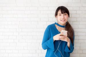 hermoso retrato mujer joven asiática de pie feliz disfrutar y divertirse escuchar música con auriculares sobre fondo de hormigón de cemento, estilo de vida de chica relajar radio de sonido con auriculares, concepto de tecnología. foto