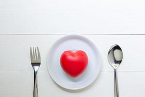 Red Heart with love and dish and spoon and fork on wooden background, 14 February Valentine day, on grunge white wood, celebration and holiday concept, top view. photo