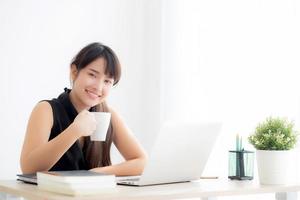 Hermosa joven mujer asiática independiente sonriendo trabajando y en una computadora portátil en la oficina de escritorio con una chica profesional que usa un cuaderno y bebe café, negocios y concepto de estilo de vida. foto