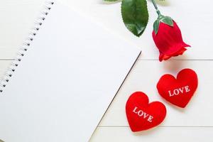 presente flor de rosa roja y cuaderno y forma de corazón con espacio para copiar en una mesa de madera, 14 de febrero del día del amor con un concepto romántico de vacaciones de San Valentín. foto