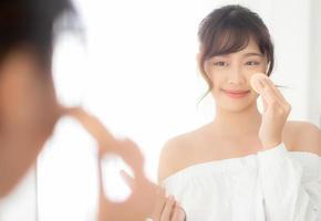 Portrait beautiful young asian woman applying powder puff at cheek makeup of cosmetic looking mirror, beauty of girl with skin face smile in the bedroom, health and wellness concept. photo