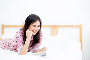 Beautiful of portrait asian young woman lying relax and leisure with laptop internet online on vacation in bedroom, cheerful of asia girl with gesture glad and success, lifestyle concept. photo