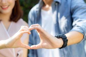 primer plano de una pareja feliz divertida haciendo gestos en forma de corazón con la mano al aire libre juntos, hombre y mujer con relación sintiendo amor con símbolo y signo, amante y concepto romántico. foto