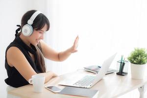 hermosa joven asiática usa auriculares sonriendo saluda usando una videollamada de chat en una computadora portátil, la chica se relaja y disfruta escuchando música en línea, educación, aprendizaje, comunicación y concepto de estilo de vida. foto