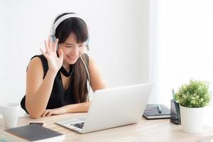 hermosa joven asiática usa auriculares sonriendo saluda usando una videollamada de chat en una computadora portátil, la chica se relaja y disfruta escuchando música en línea, educación, aprendizaje, comunicación y concepto de estilo de vida. foto