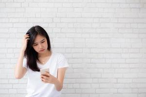 Portrait of asian woman have bored and displeased with something looking smart phone standing on cement brick background, girl with expression and emotion, lady tired or problem. photo