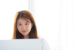 Portrait of beautiful asian young woman setting on bed using laptop computer at bedroom for leisure and relax, freelance with girl working notebook, communication and lifestyle concept. photo