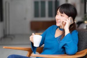 Beautiful portrait young asian woman smiling using mobile smart phone talking enjoy and drink coffee with relax, girl sitting on chair, communication concept. photo