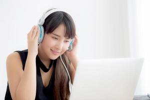 Beautiful young asian woman wear headphone smiling say hello using chat video call on laptop computer, girl relax enjoy listening music online, education learning, communication and lifestyle concept. photo