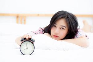 Beautiful asian young woman turn off alarm clock in morning, wake up for sleep with alarm clock, relax and lifestyle concept. photo