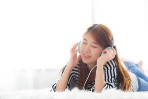 hermosa mujer joven asiática disfruta y se divierte escuchando música con auriculares en el dormitorio, la chica se relaja con el concepto de auriculares, ocio y tecnología. foto